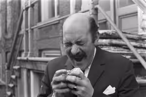 A man photographed mid-sneeze in black and white, head tipped back, from a 1960s Dutch press archive